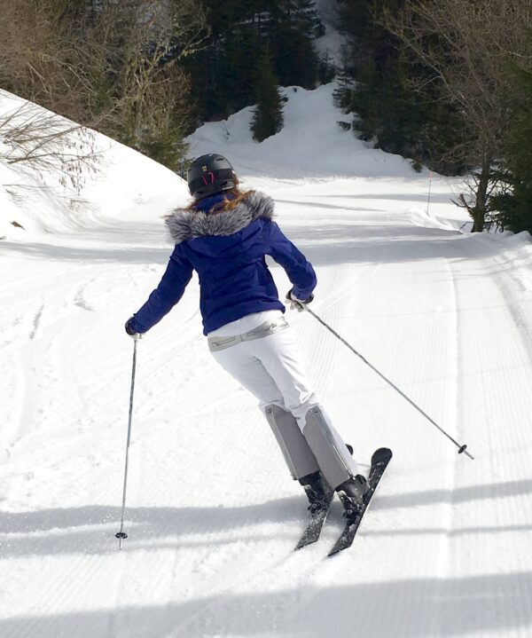 Skieuse de dos en tenue de ski blanche et bleue.